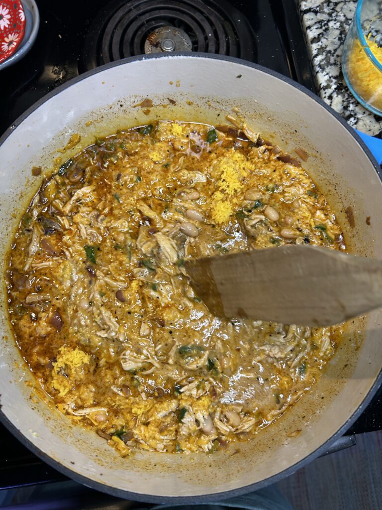 A Dutch oven with white turkey chili cooking in it while a spoon is stirring the soup