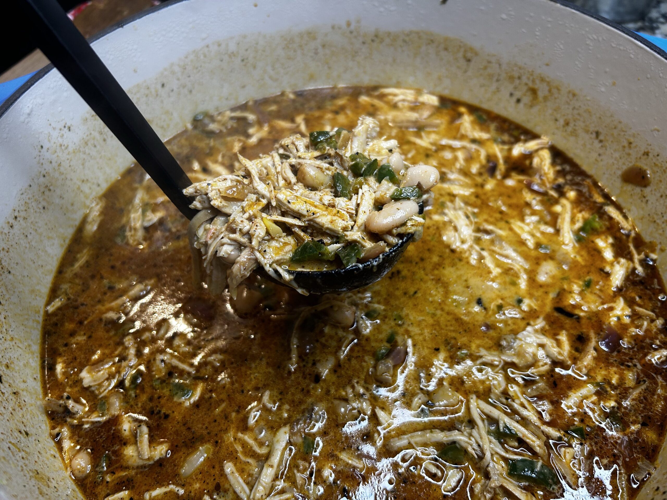 White turkey chili in Dutch oven with a ladle being used to serve soup out of the pot