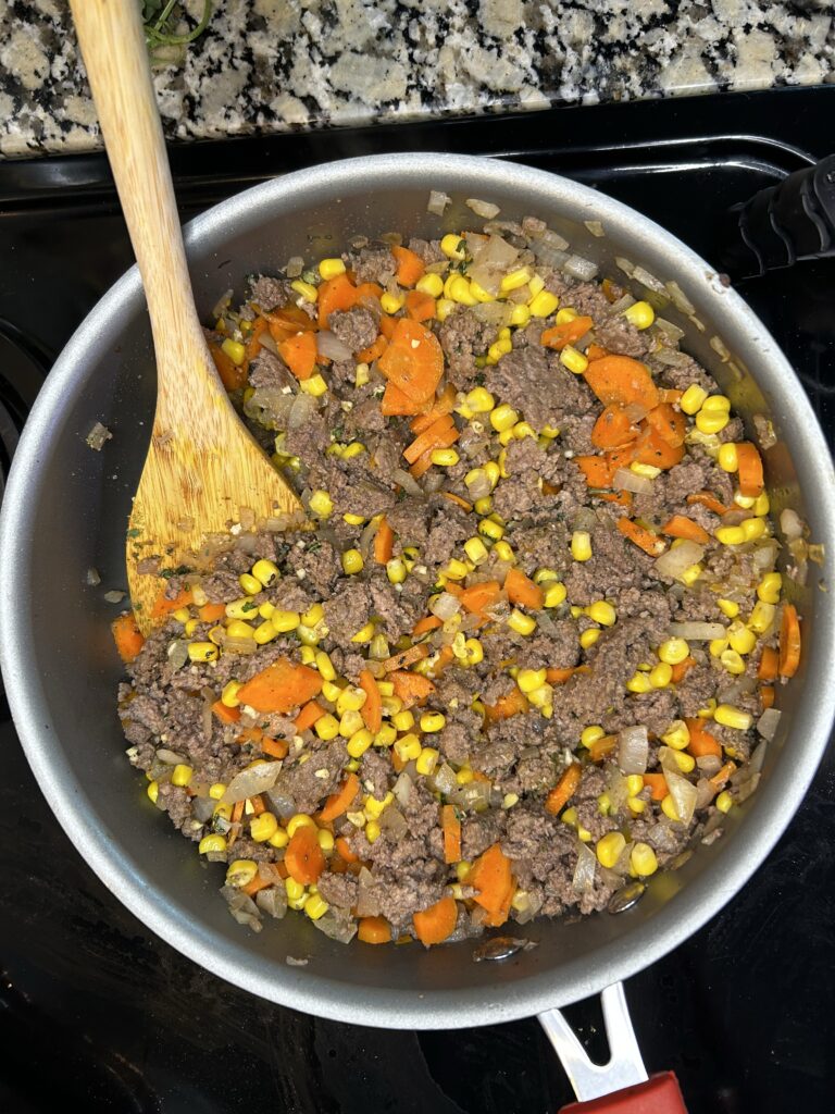 Skillet with shepherds pie filling of browned ground beef, sauteed spinach, carrots, onion, and corn