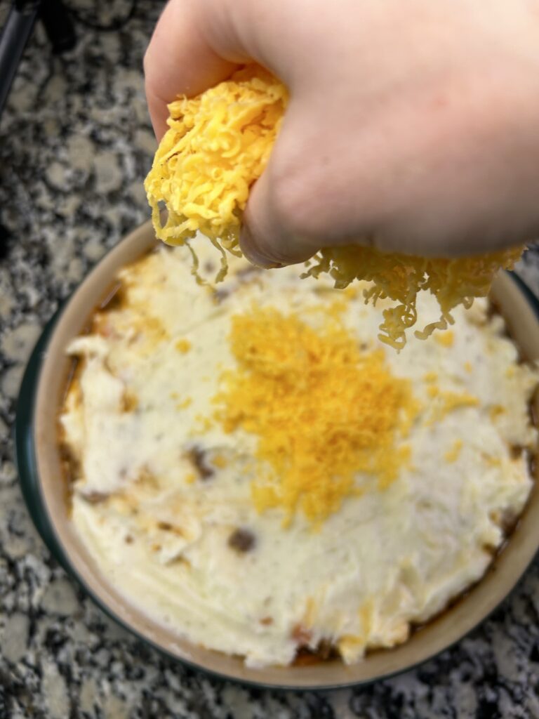 Topping shepherds pie and mashed potatoes with shredded cheddar cheese