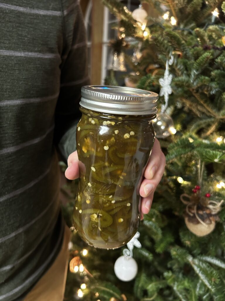 candied jalapenos in jar held in front of christmas tree