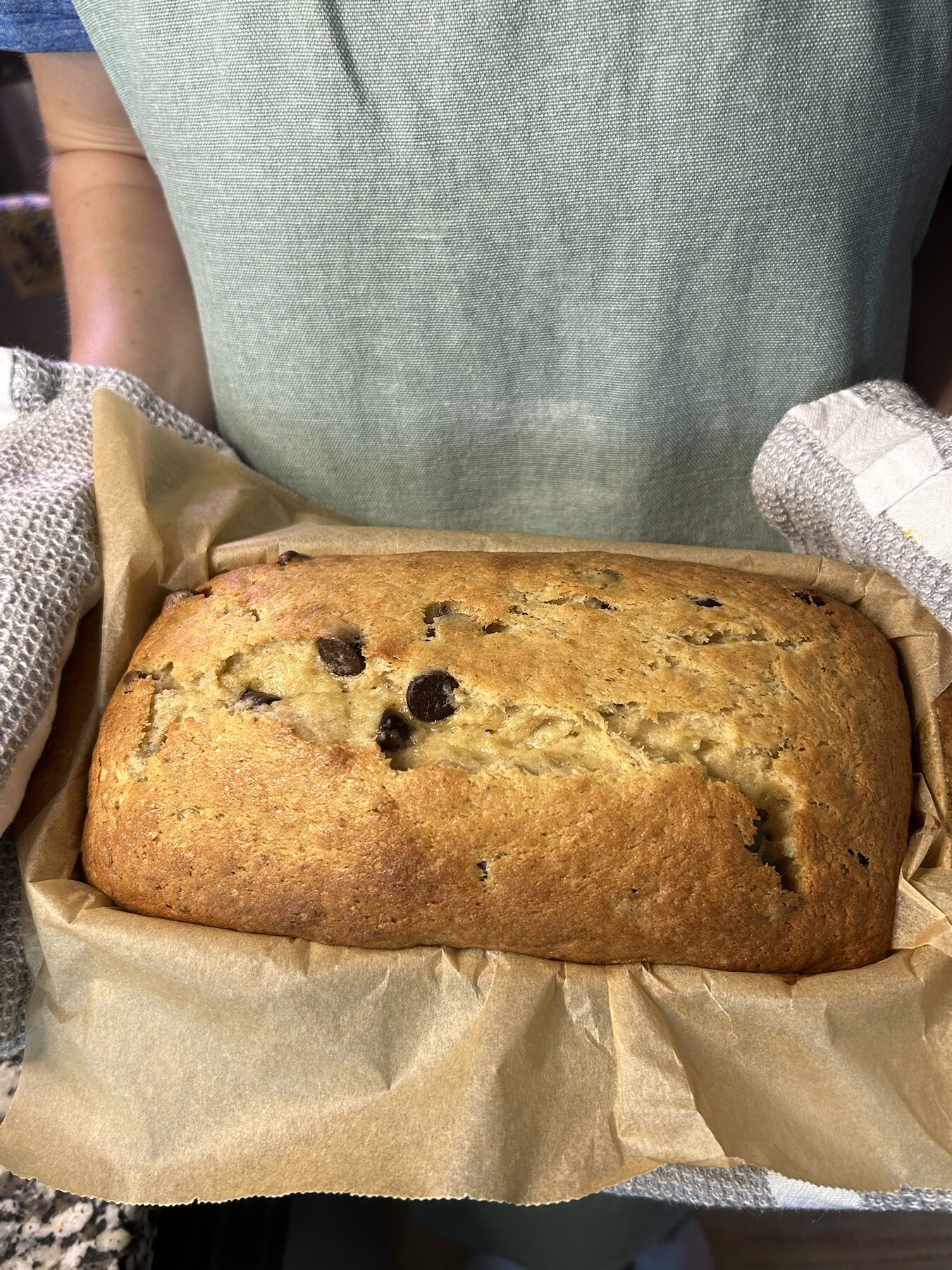 person holding chocolate chip banana bread in bread pan