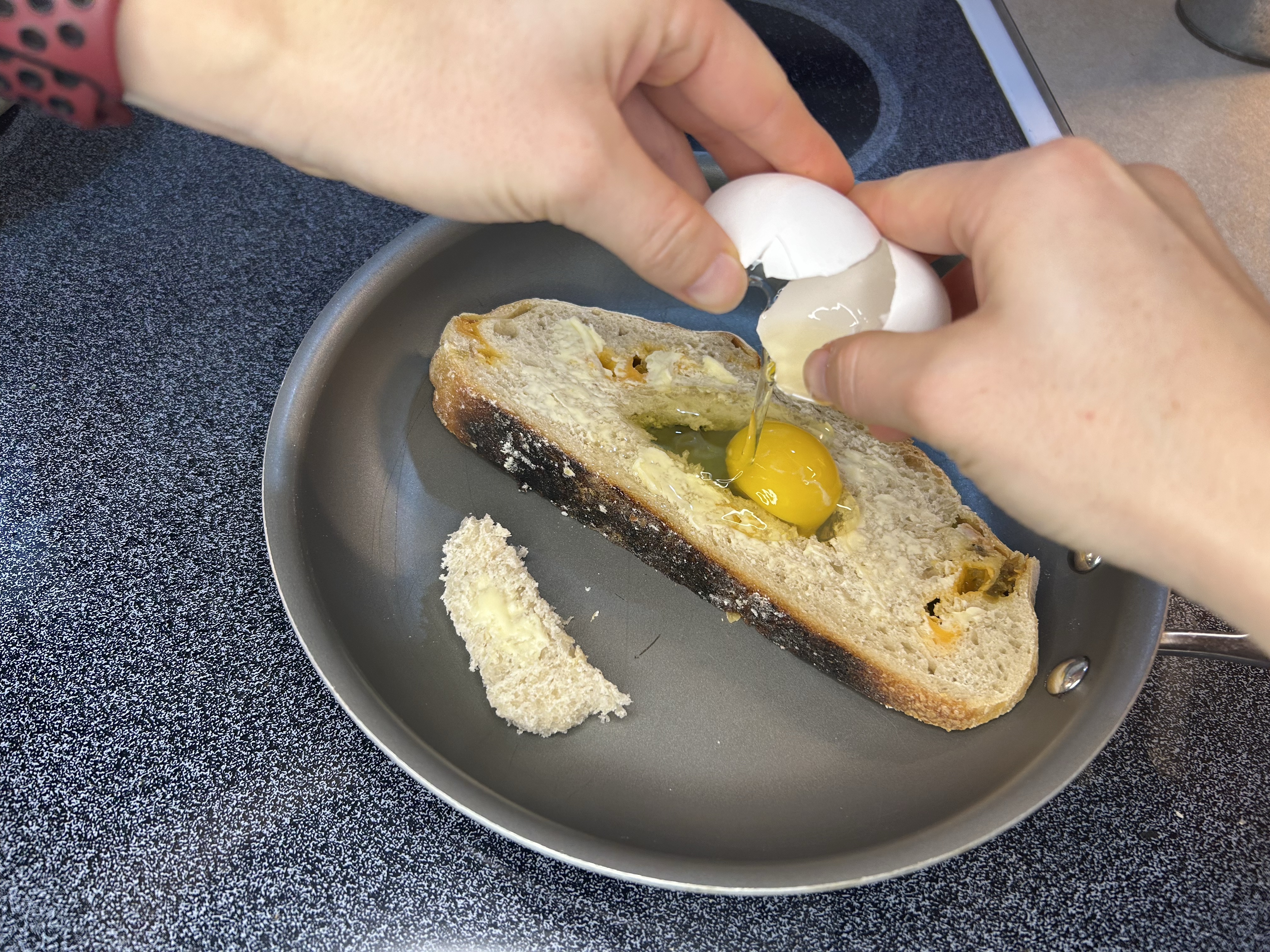 two hands cracking an egg onto toast in skillet