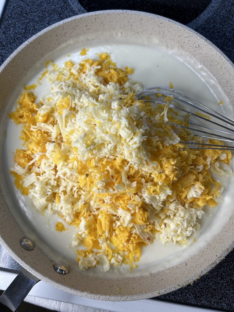 shredded cheese being added to a roux in a skillet with a whisk