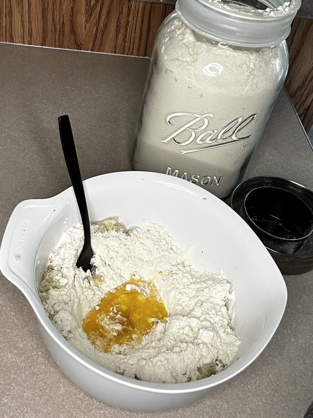 bowl with flour and egg, with mason jar of flour sitting behind bowl