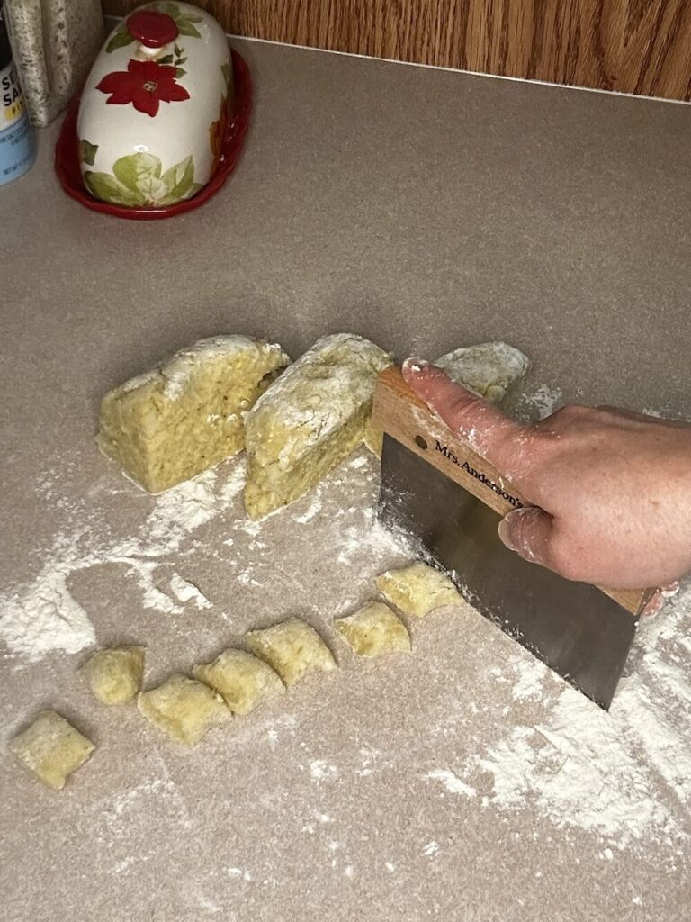 hand using bench scraper to cut homemade potato gnocchi dough into pieces
