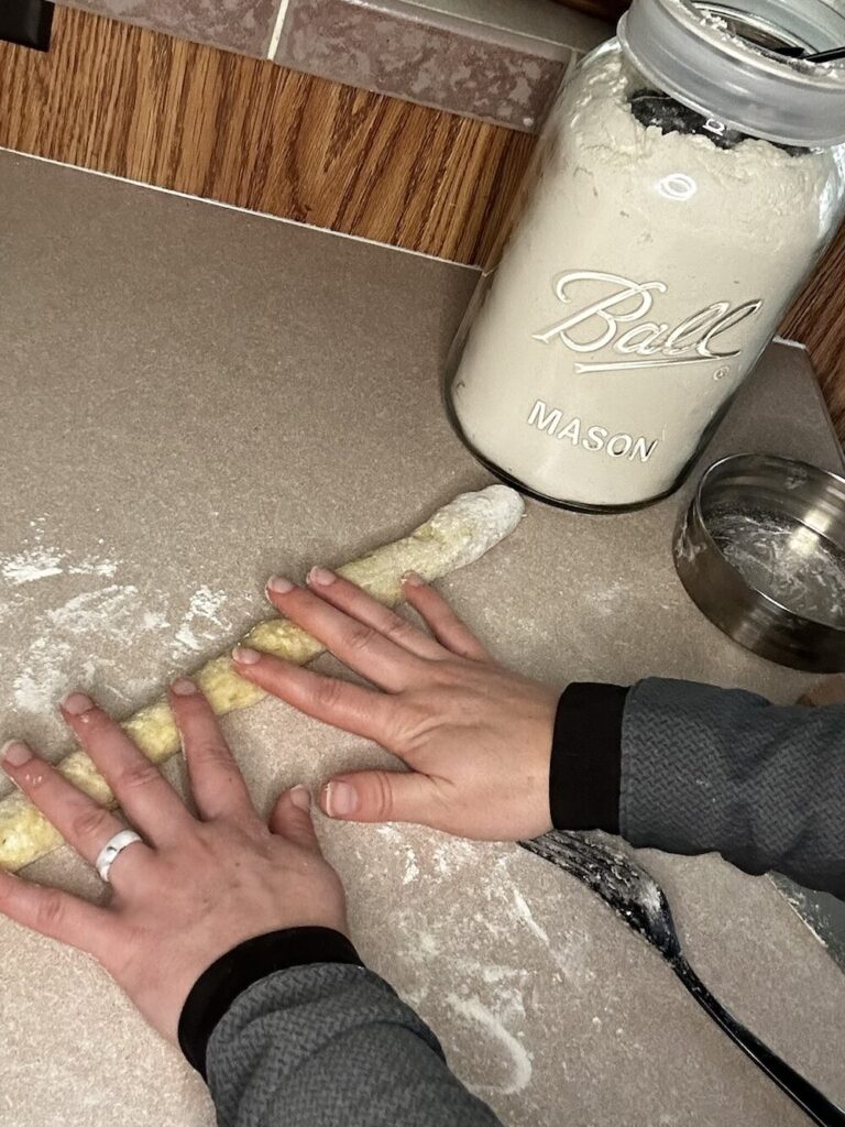 hands rolling out  homemade potato gnocchi dough into a log